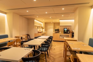 Een restaurant met meerdere tafels en stoelen, een toonbank met een koffiemachine en een televisiescherm.