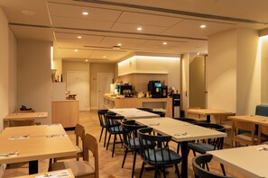 Un comedor de hotel con varias mesas y sillas, una cocina al fondo y un diseño interior moderno.