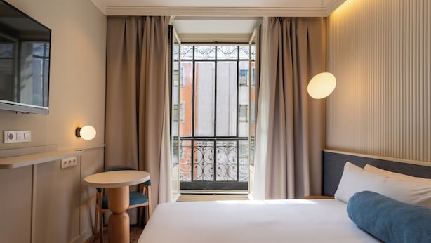 Une chambre d’hôtel avec un lit, une table ronde, une télévision et une fenêtre avec des rideaux.