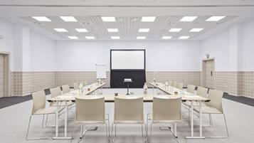 Een vergaderzaal met een lange tafel, stoelen, een projectiescherm en een whiteboard.