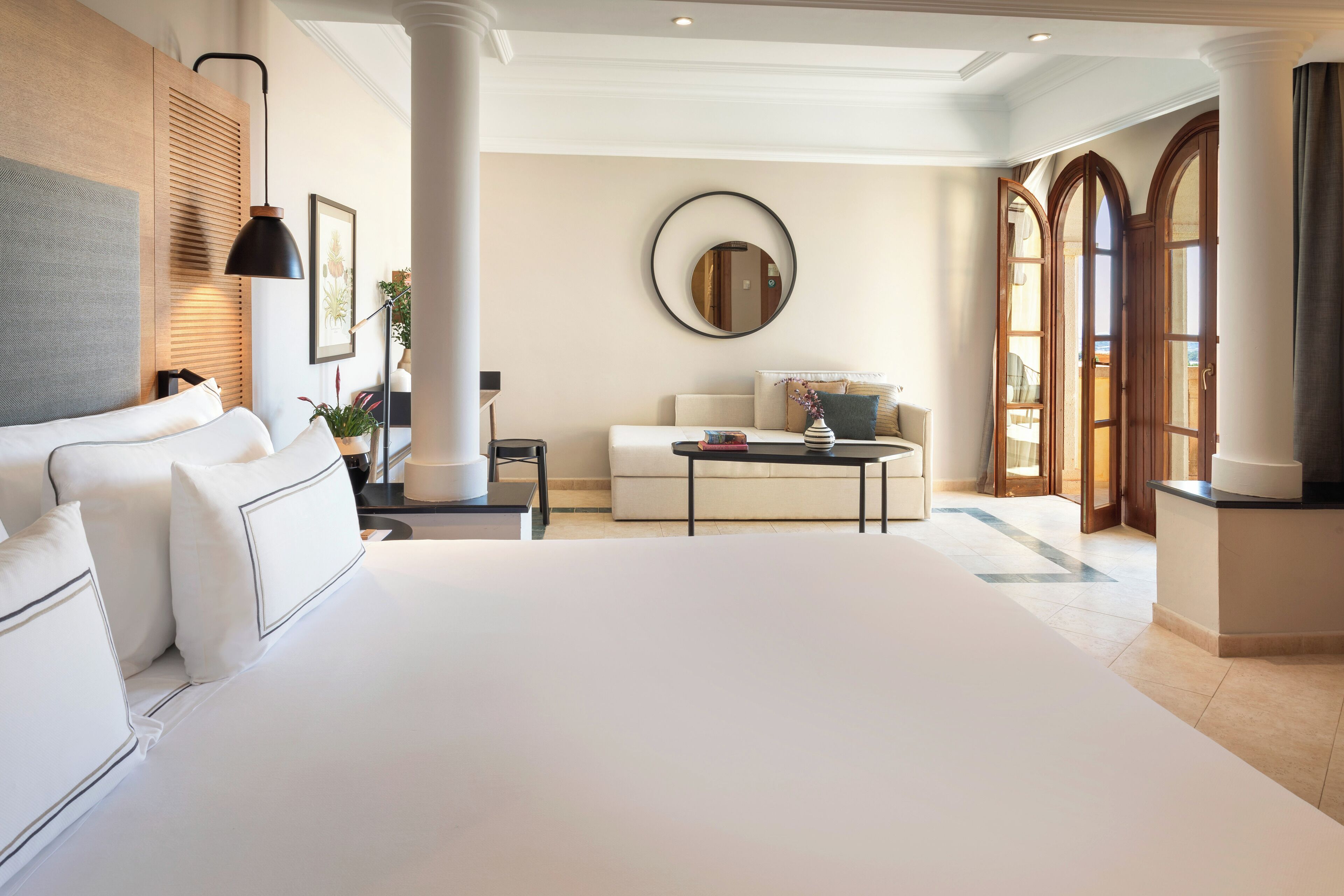 Un dormitorio amplio con una cama grande, una zona de estar con sofá y mesa de centro, y vistas a un área exterior a través de un ventanal.