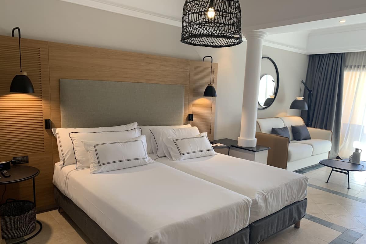 A hotel room with a double bed, a sofa, a small table, and a hanging light fixture.