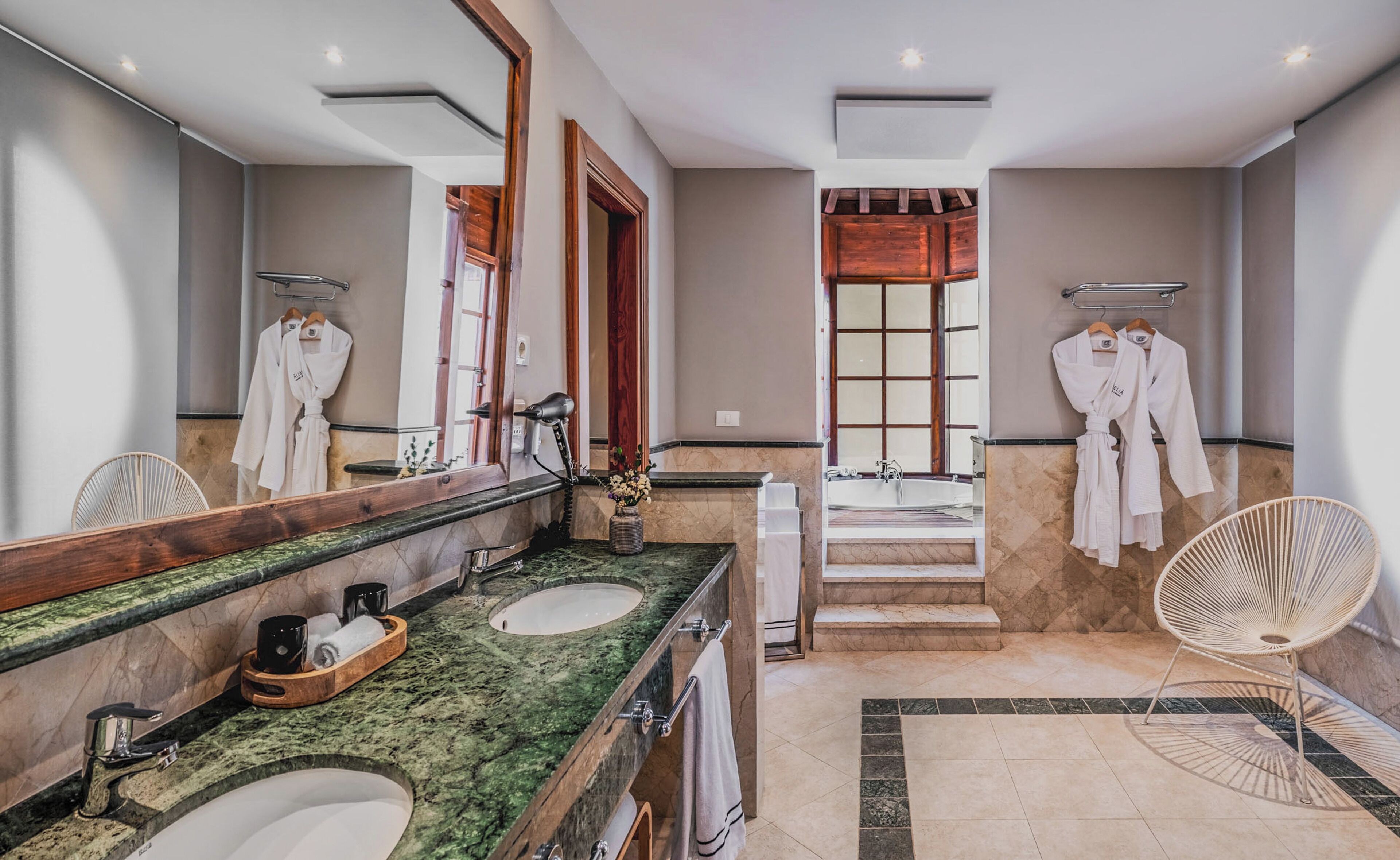 A modern bathroom with two sinks, a large mirror, a hairdryer, and a window with wooden shutters.