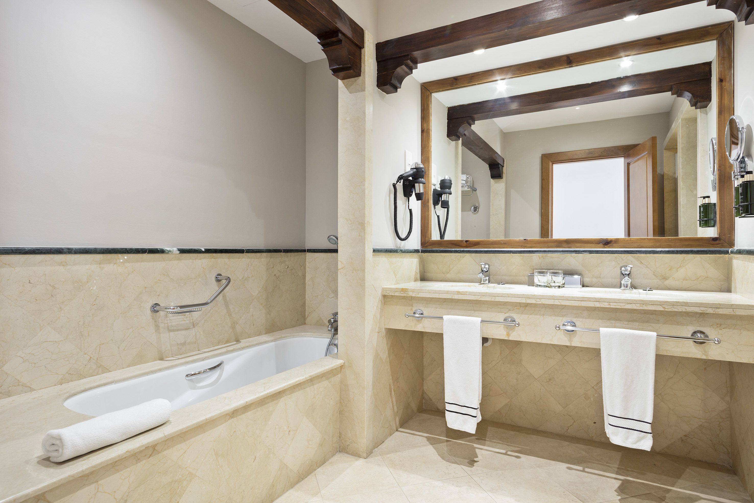 Un baño con bañera, tocador con espejo y dos toallas colgadas en el perchero.