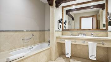 Un baño con bañera, tocador con espejo y dos toallas colgadas en el perchero.