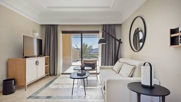 A modern hotel room with a sofa, a TV, a small table, and a balcony with a view.