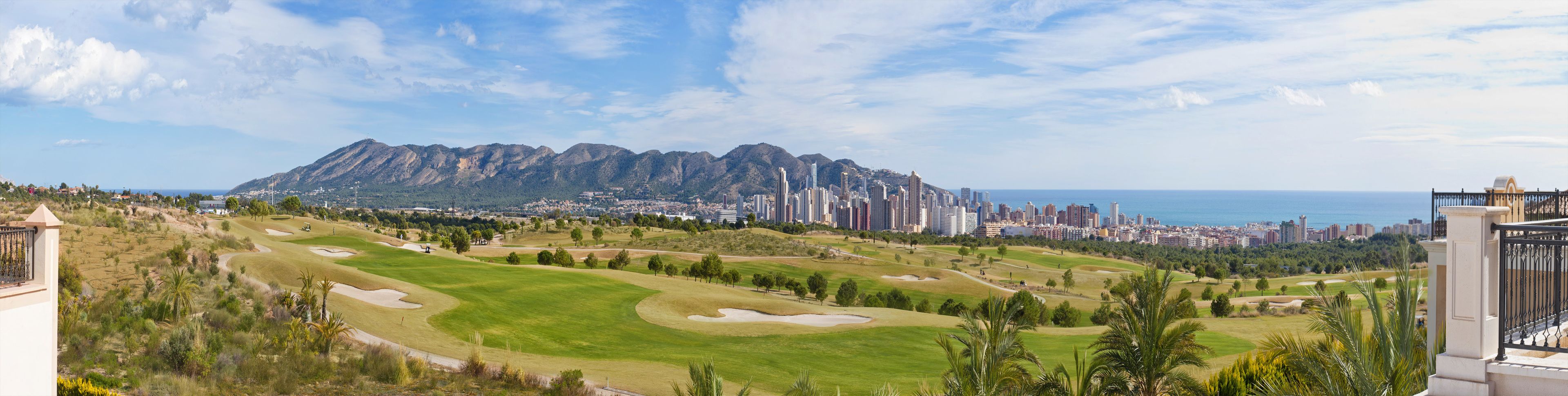 Een golfbaan met een stadsachtergrond en bergen op de achtergrond.