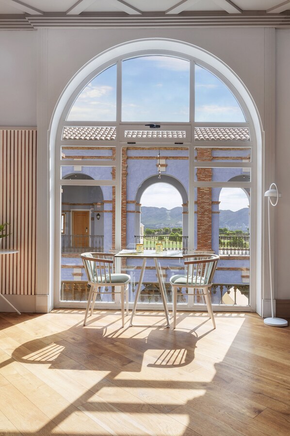 Quarto com uma grande janela em arco com vista para uma paisagem deslumbrante, piso de madeira e uma mesa com cadeiras.