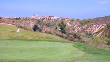Campo de golf con un marcador de bandera en primer plano, un césped bien cuidado y un edificio con tejado rojo al fondo.