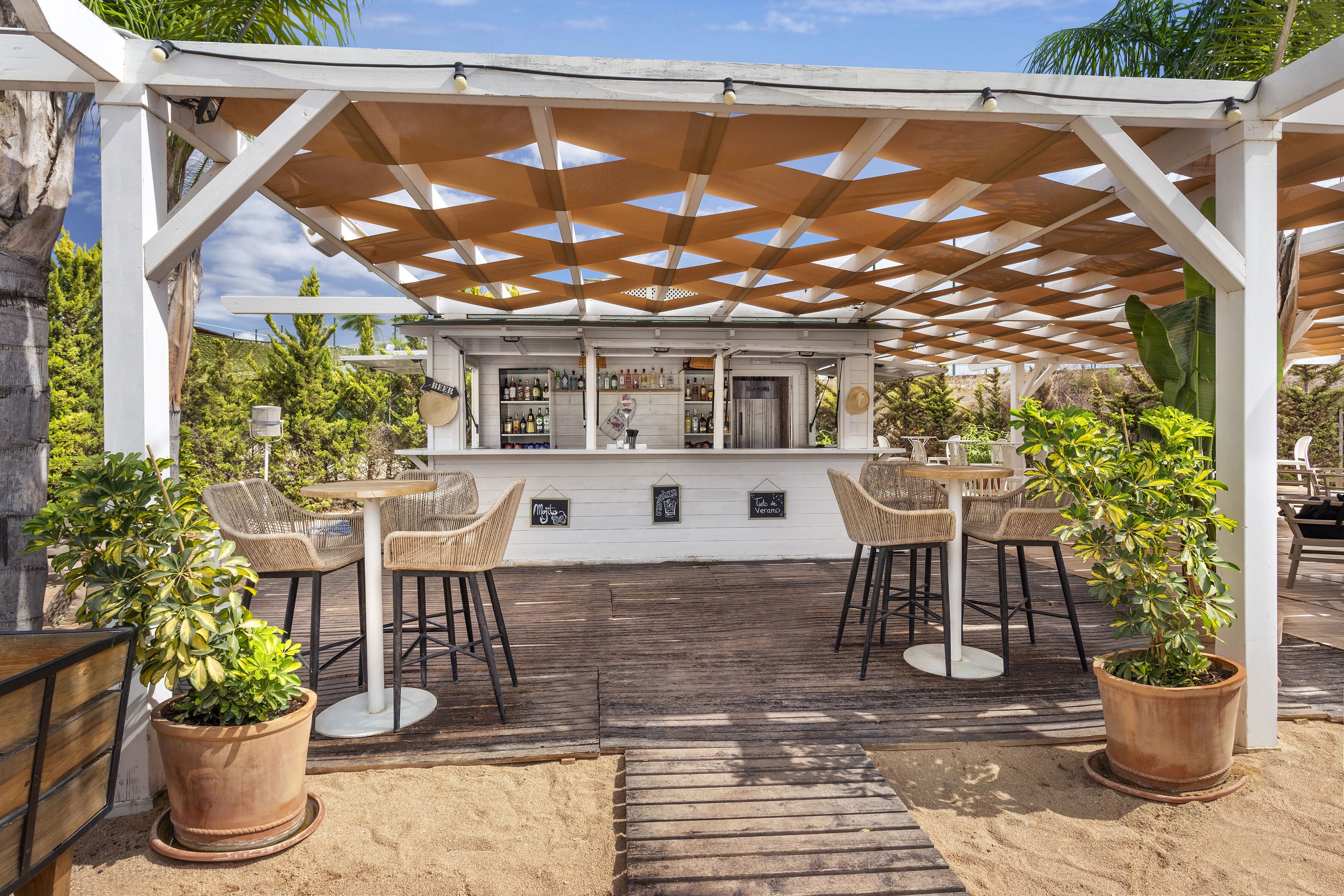 A covered outdoor bar area with wooden flooring, wicker chairs, and potted plants.