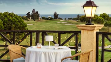 Una mesa redonda con mantel blanco, dos sillas de mimbre, una lámpara de mesa y luces decorativas en un balcón con vistas a un campo de golf.