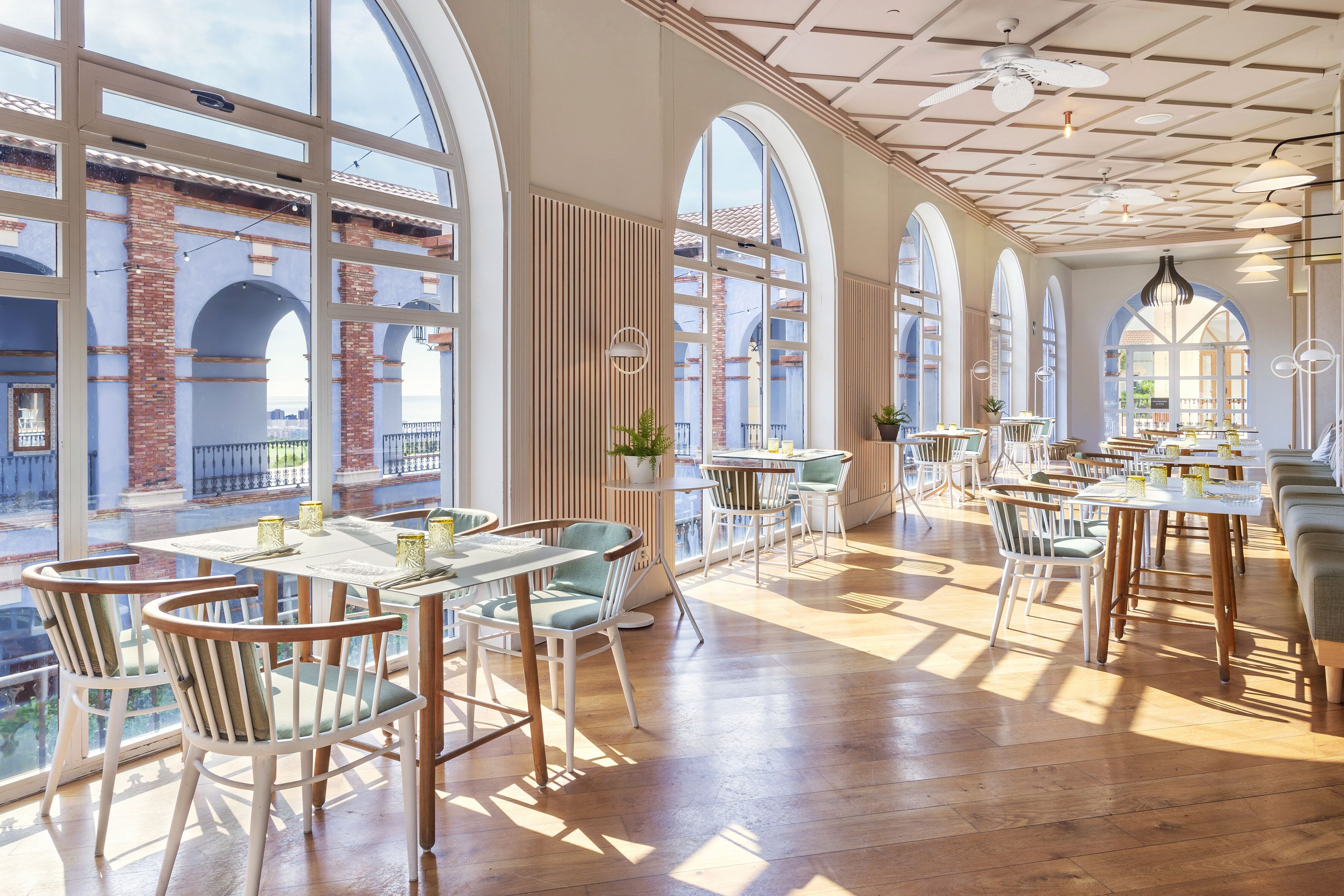 A spacious restaurant with high ceilings, large windows, and a mix of wooden and upholstered chairs.