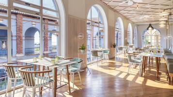 A spacious restaurant with high ceilings, large windows, and a mix of wooden and upholstered chairs.