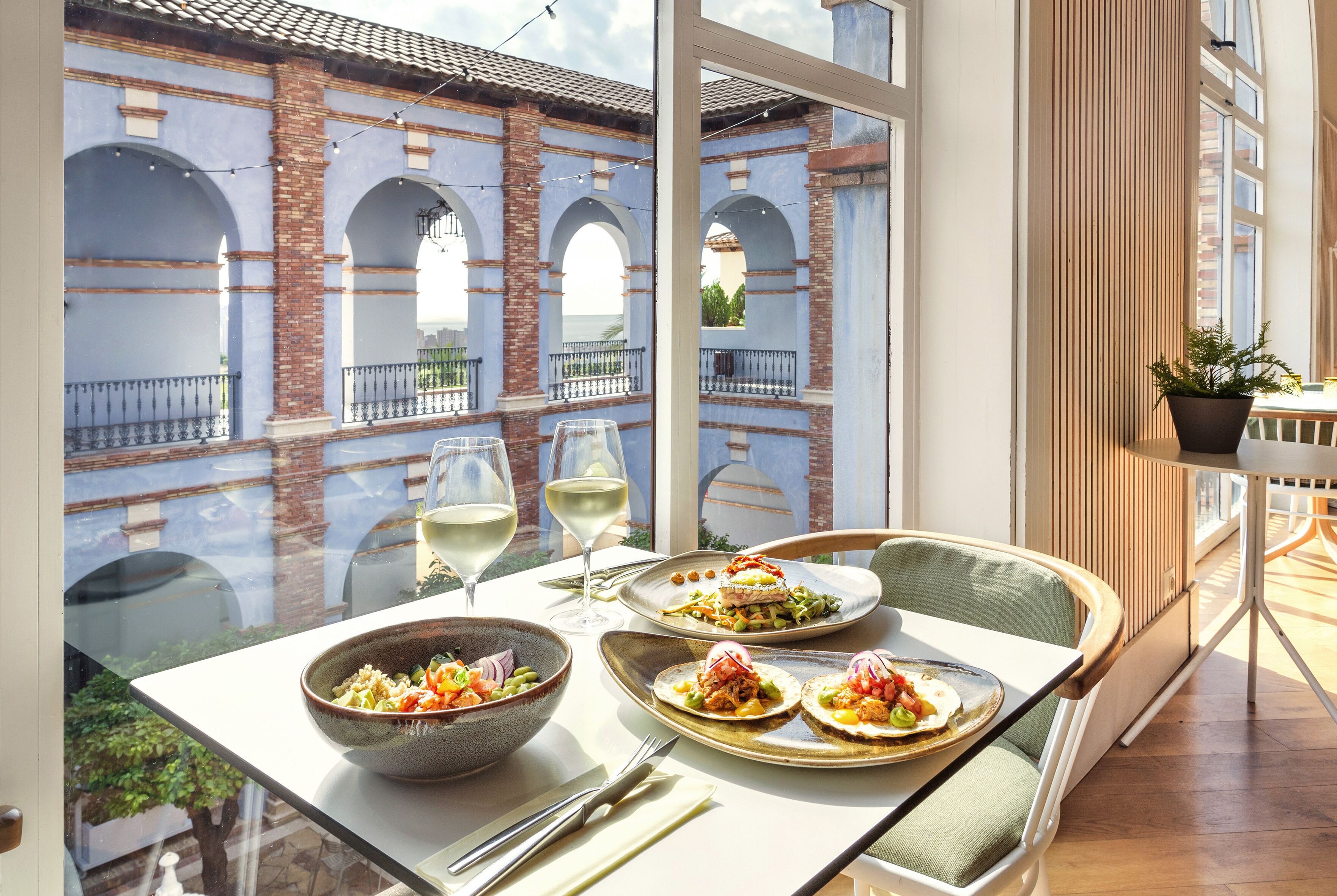 Una mesa de comedor con platos de comida, copas de vino y cubiertos.