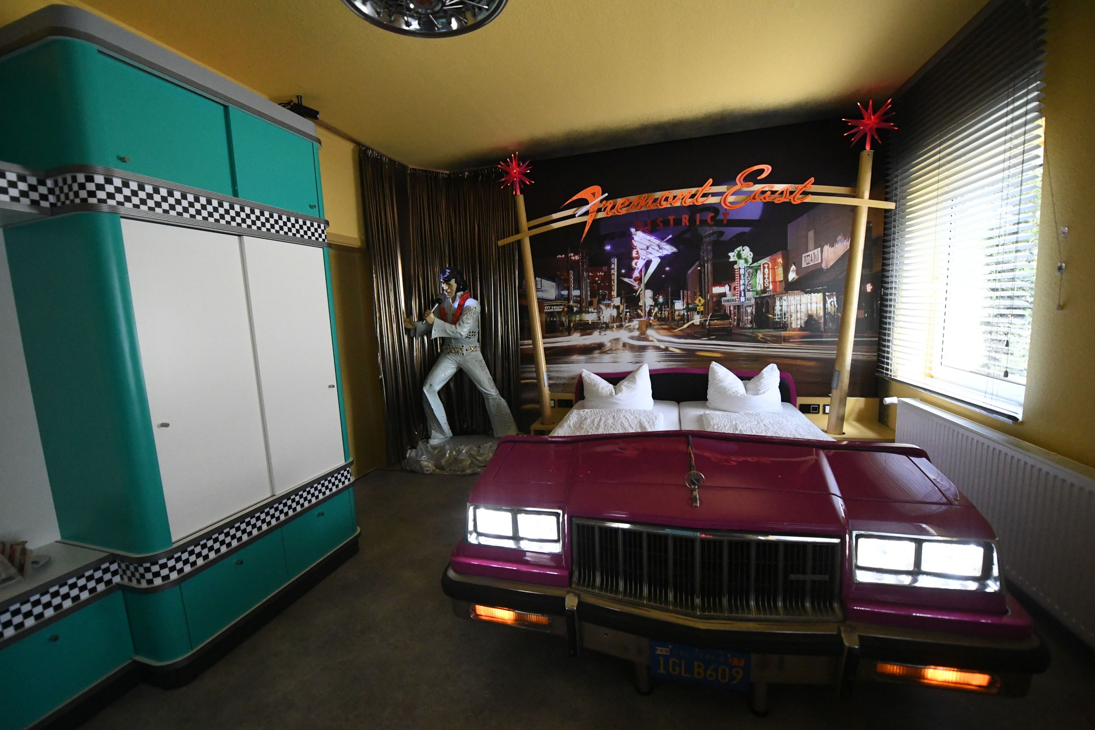 Ein Zimmer mit einem Oldtimer, einer Neonreklame und einem Schachbrettmuster auf den Möbeln.