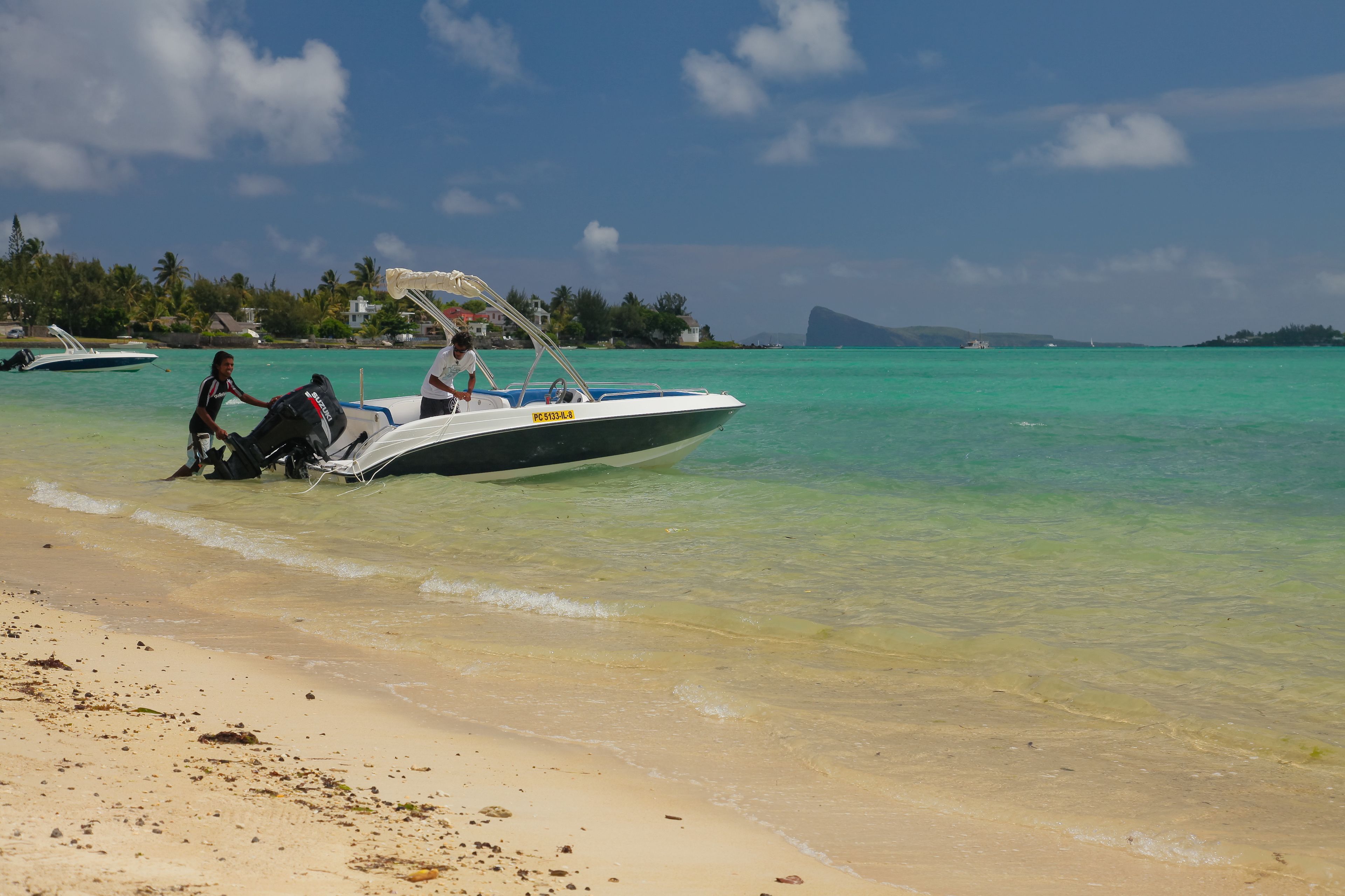 Een boot op het strand met helder turquoise water en een eiland in de verte.
