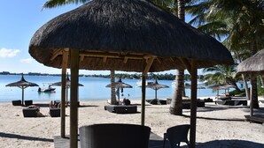 Una playa con sombrillas de paja, sillas reclinables y una cubierta de madera.