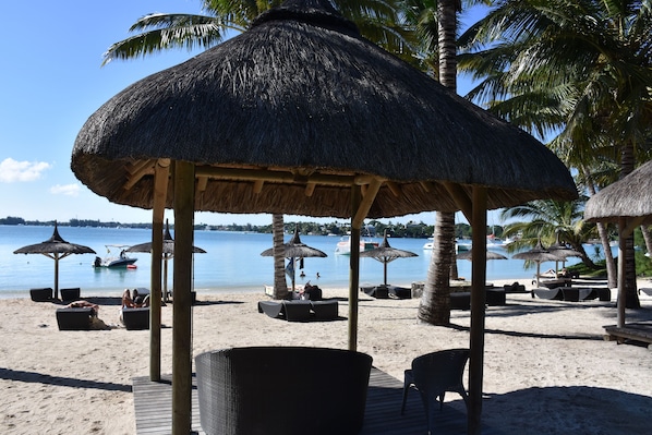 Una playa con sombrillas de paja, sillas reclinables y una cubierta de madera.
