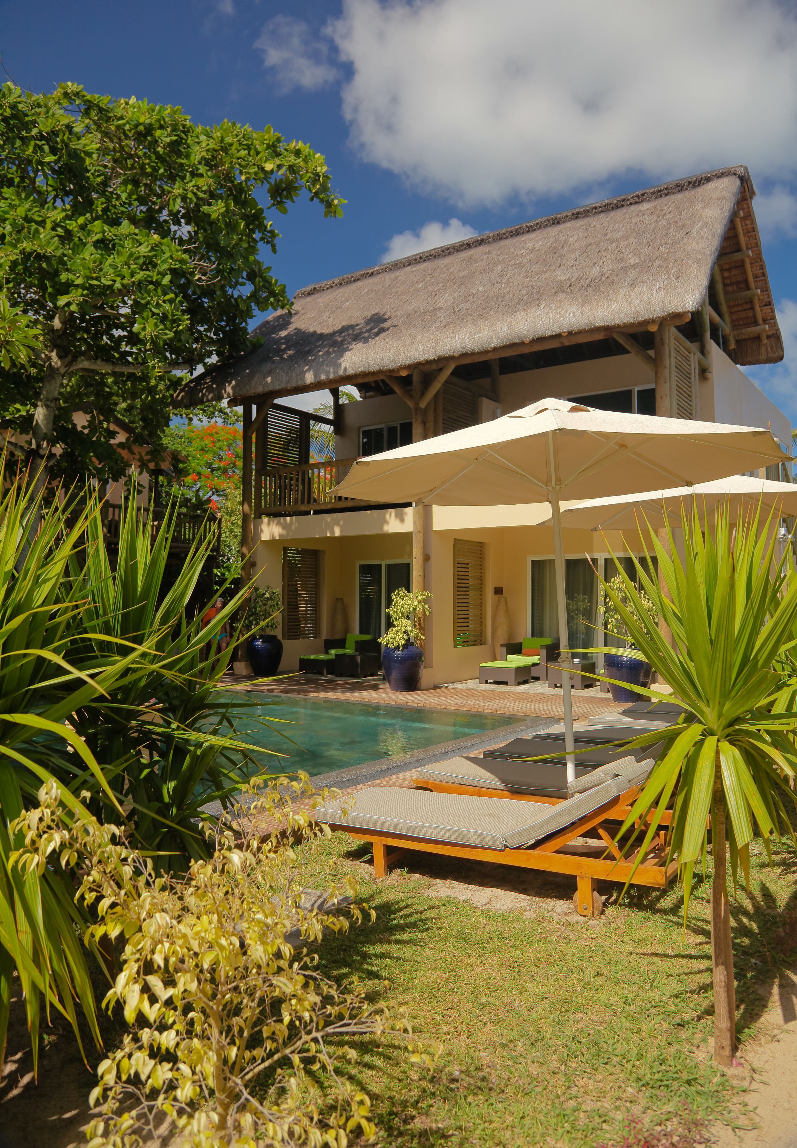 A two-story building with a pool, outdoor seating, and tropical plants.