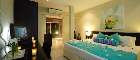 Una habitación de hotel con cama, mesita de noche, televisión y vista al pasillo.