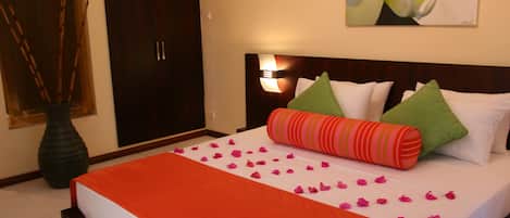 Una habitación de hotel con cama, almohadas, un florero y una lámpara de pared.