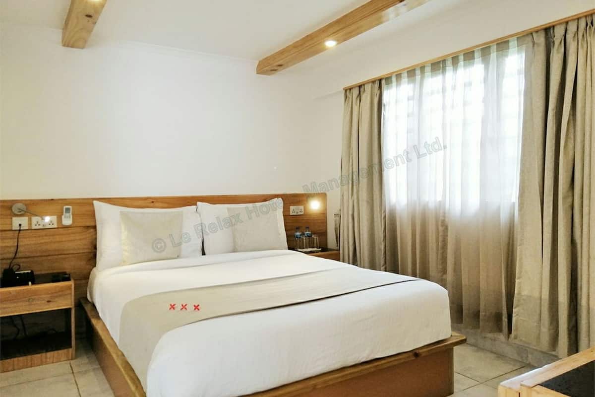 A hotel room with a wooden headboard, a large bed with white bedding, a bedside table with a lamp, and a window with curtains.