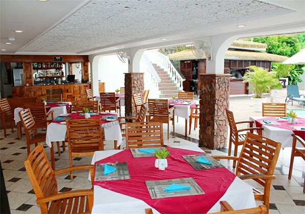 Un restaurante con mesas y sillas de madera, una zona de bar y una escalera que sube a un nivel superior.