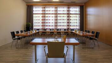 Une salle de conférence avec une longue table, des chaises et une grande fenêtre équipée de stores.