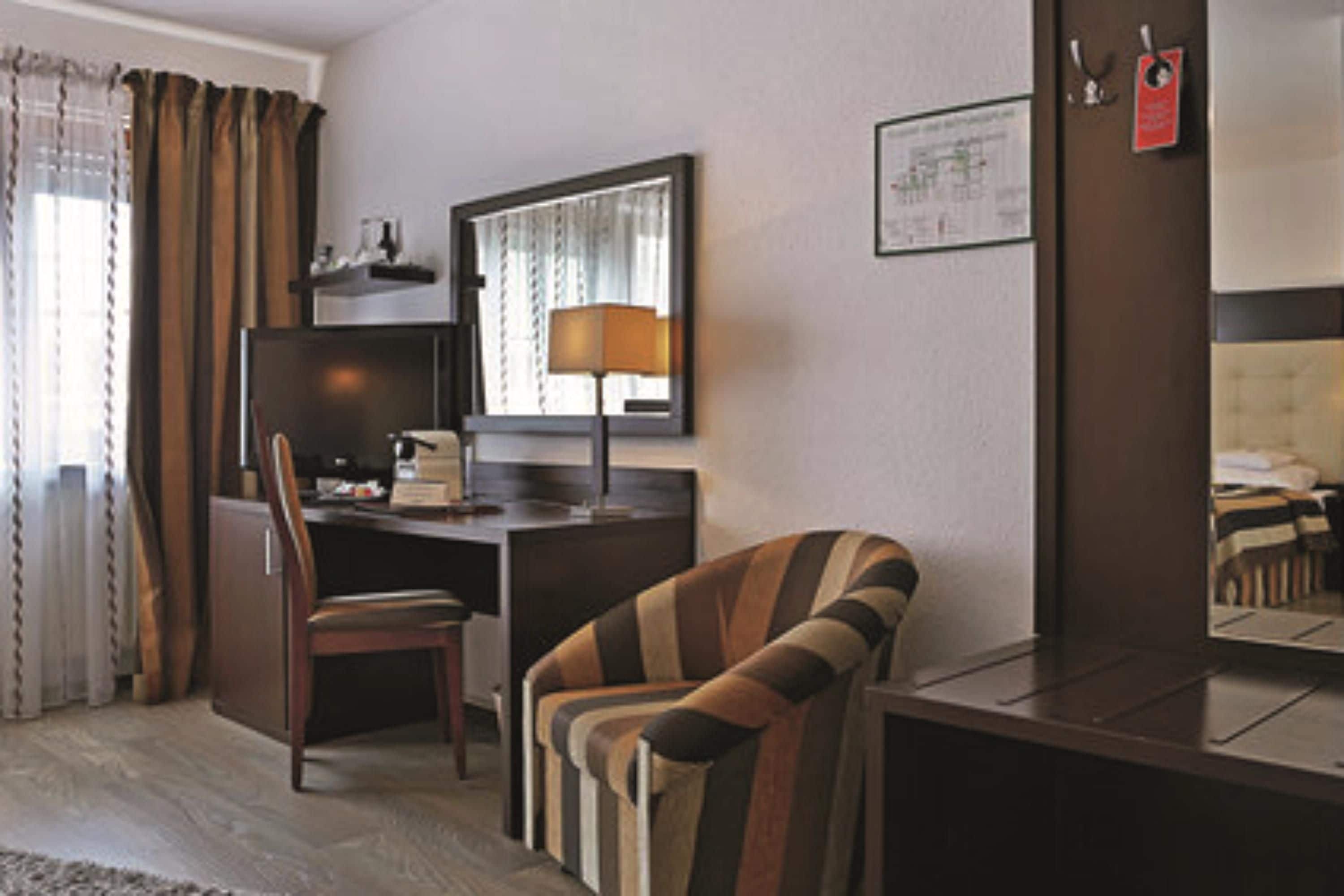 Habitación de hotel con escritorio, silla y sillón a rayas.