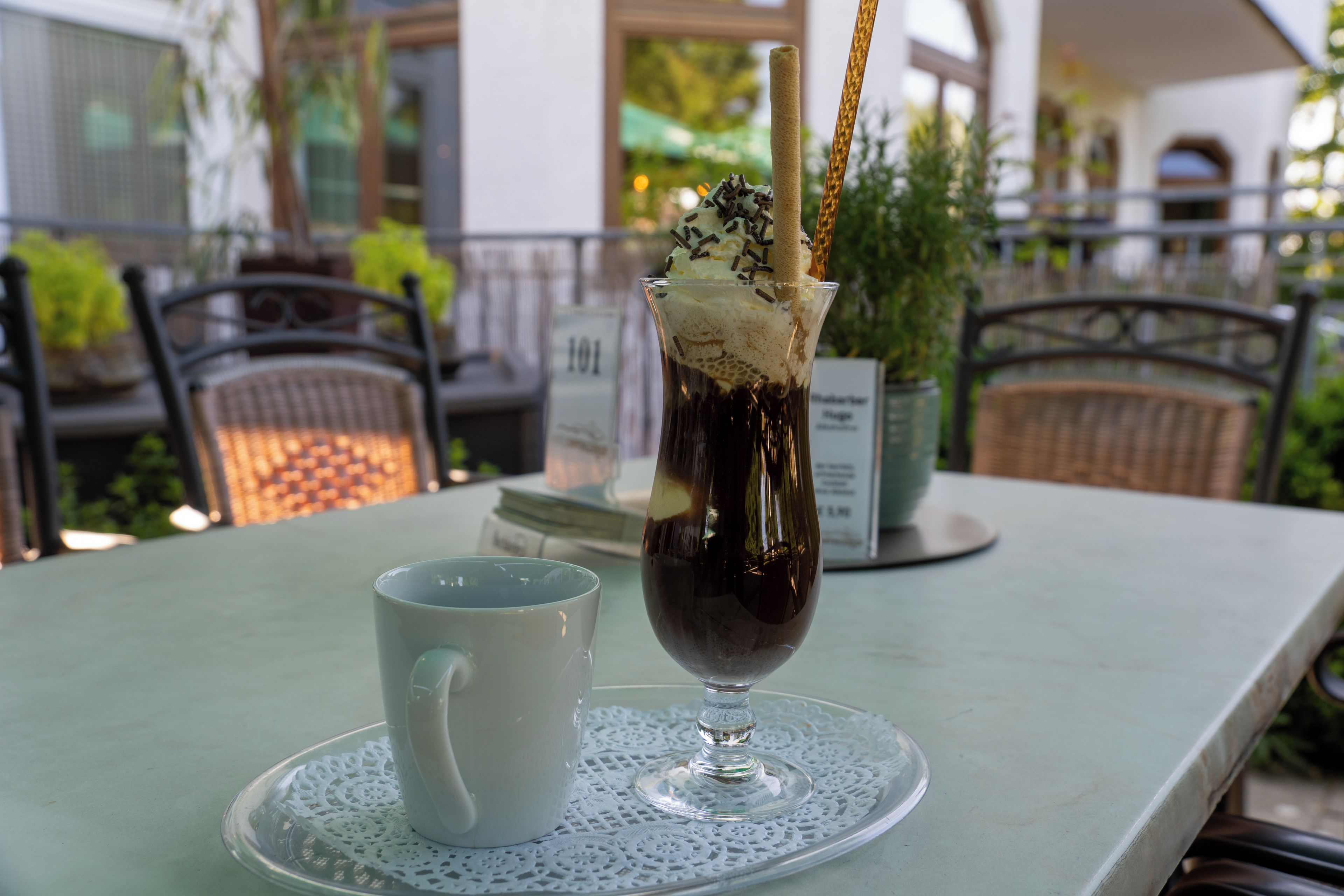 A table with a glass of iced coffee, a white mug, and a menu sign in the background.