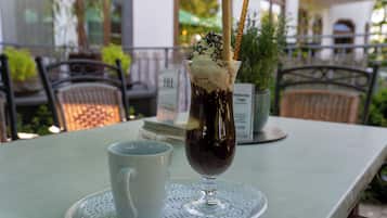 Una mesa con un vaso de café helado, una taza blanca y un cartel de menú al fondo.