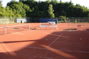 Una cancha de tenis con red, bancos y una valla.