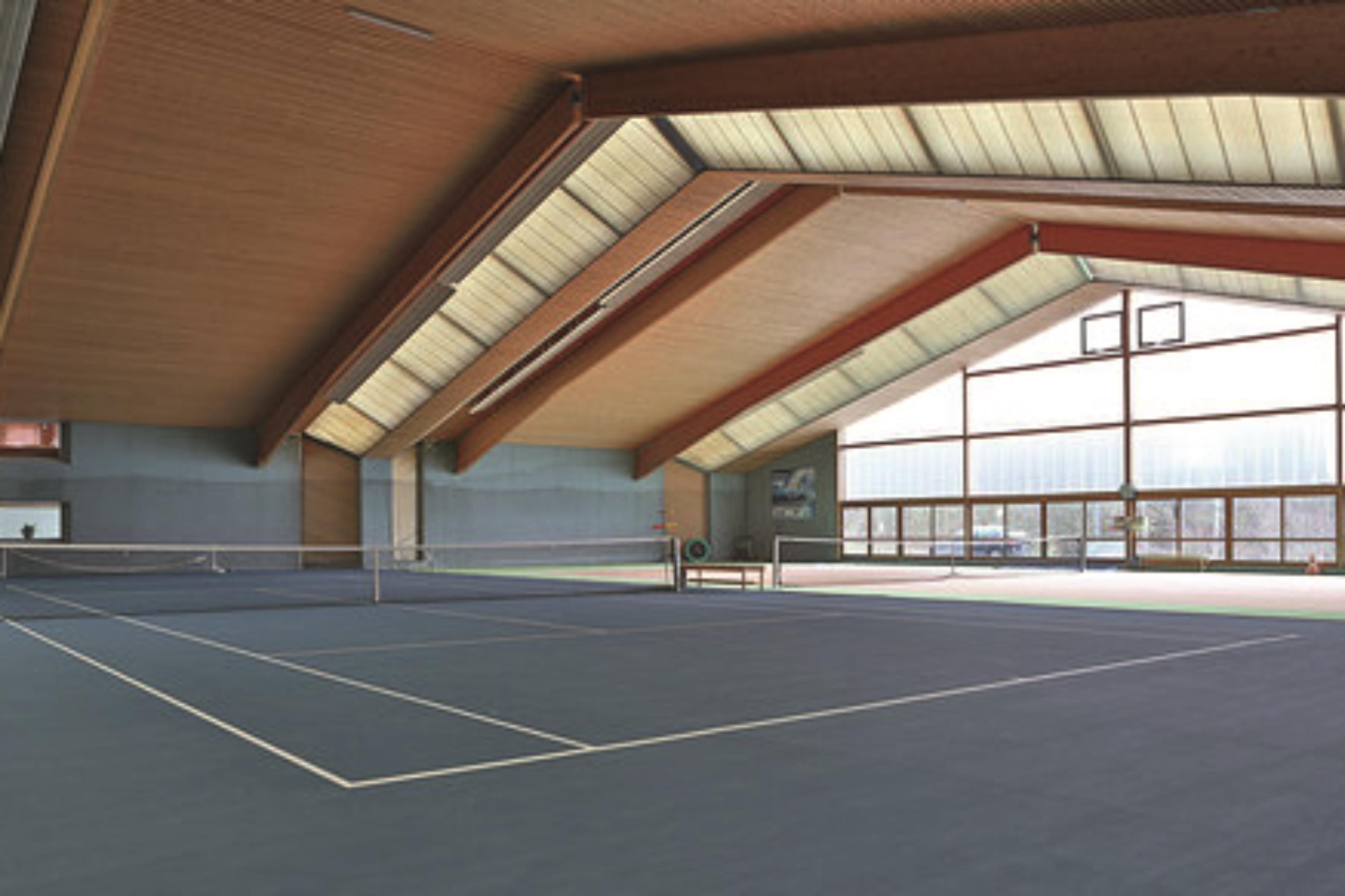 Pista de tenis interior con techo alto y ventanas amplias.