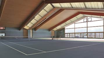 Pista de tenis interior con techo alto y ventanas amplias.
