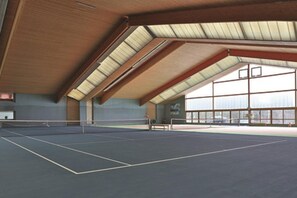 An indoor tennis court with a high ceiling and large windows.