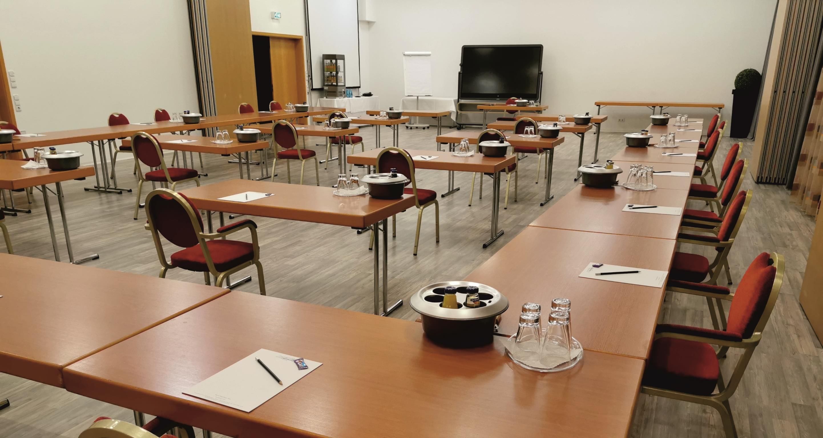 Un salón de conferencias con varias mesas, sillas, una pantalla de proyector y una pizarra.