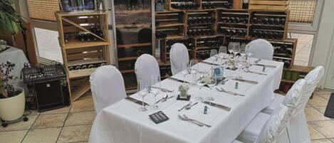 Un comedor con una mesa larga dispuesta para una comida, rodeado de botelleros.