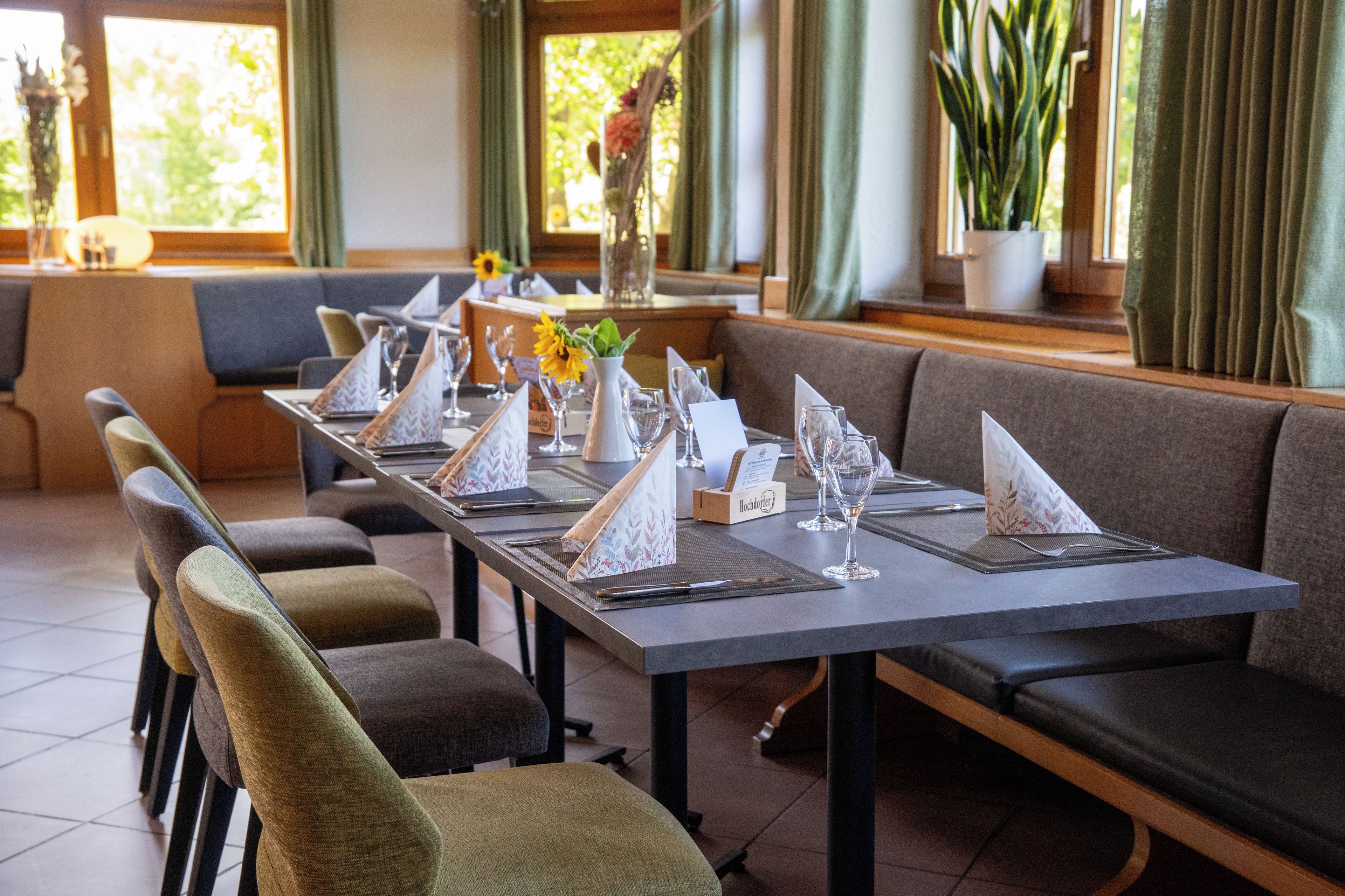 Un restaurante con una larga mesa dispuesta para comer, asientos acolchados y un jarrón con flores.