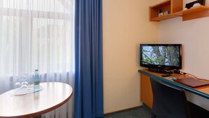 A hotel room with a round table, a television, a blue curtain, and a shelf with items. - Hotel Empfinger Hof, Sure Hotel Collection by Best Western (Empfingen)