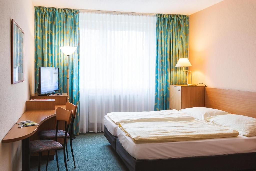 Een hotelkamer met een bed, bureau, stoel, televisie en gordijnen.