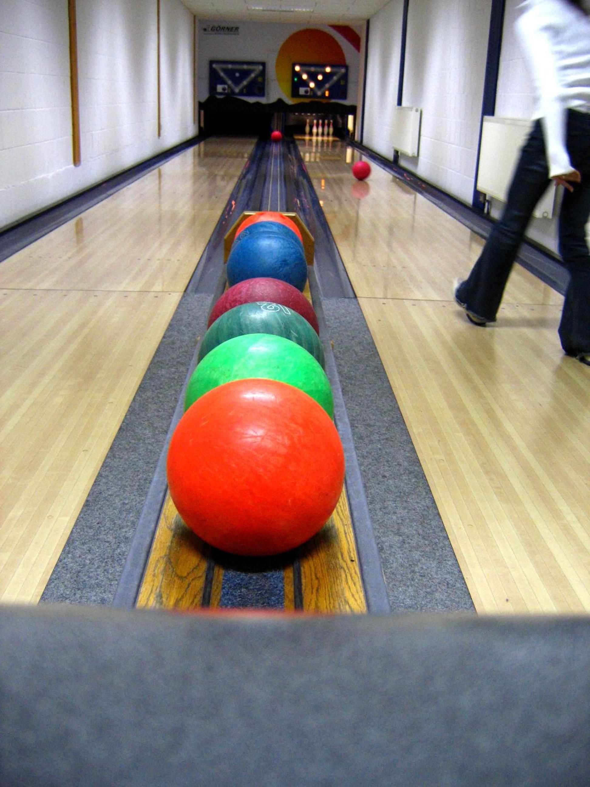 Une salle de bowling avec une piste délimitée par des boules de couleur et une personne en mouvement.