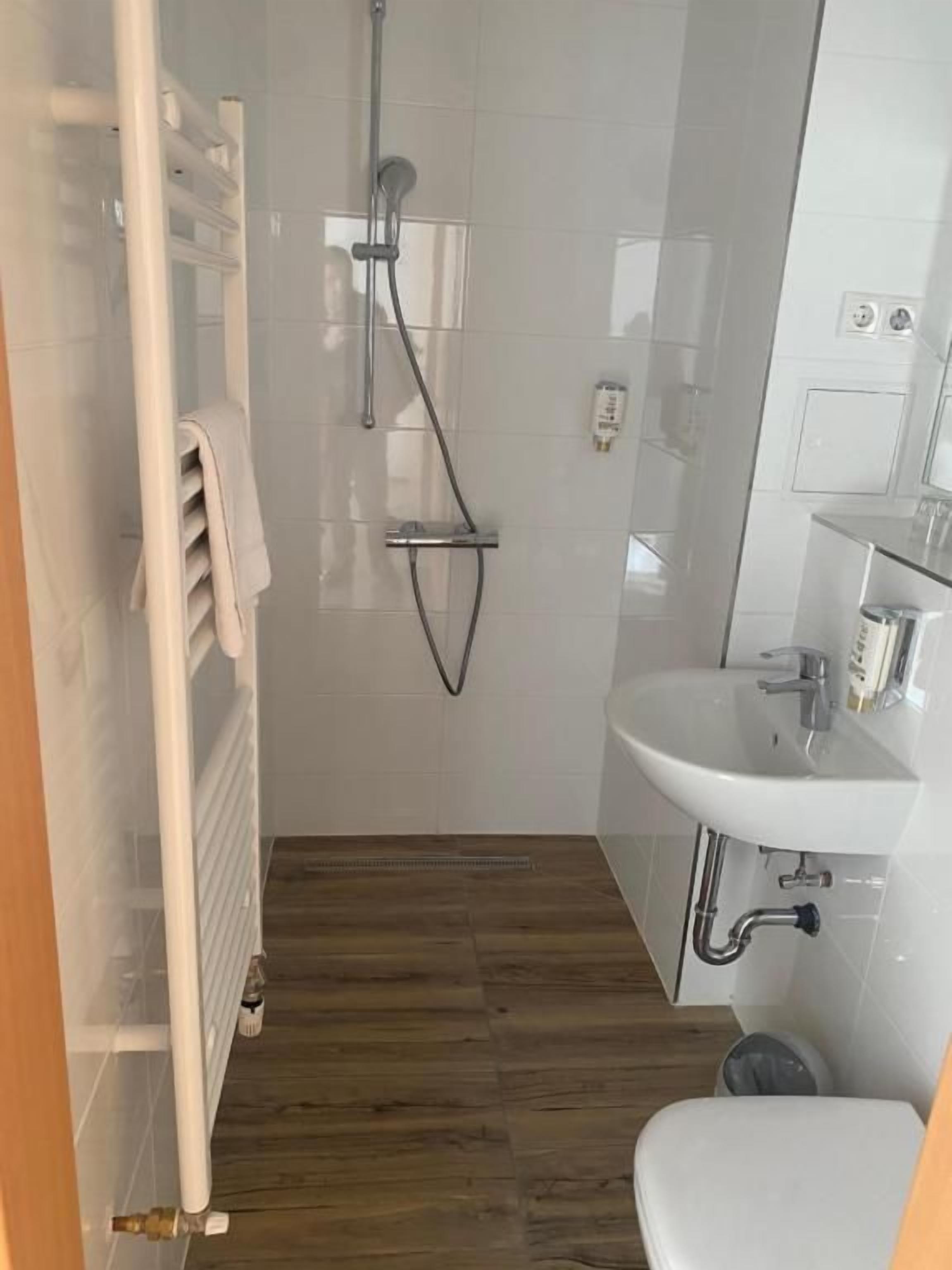 A bathroom with a shower, a toilet, a sink, and a towel rack.