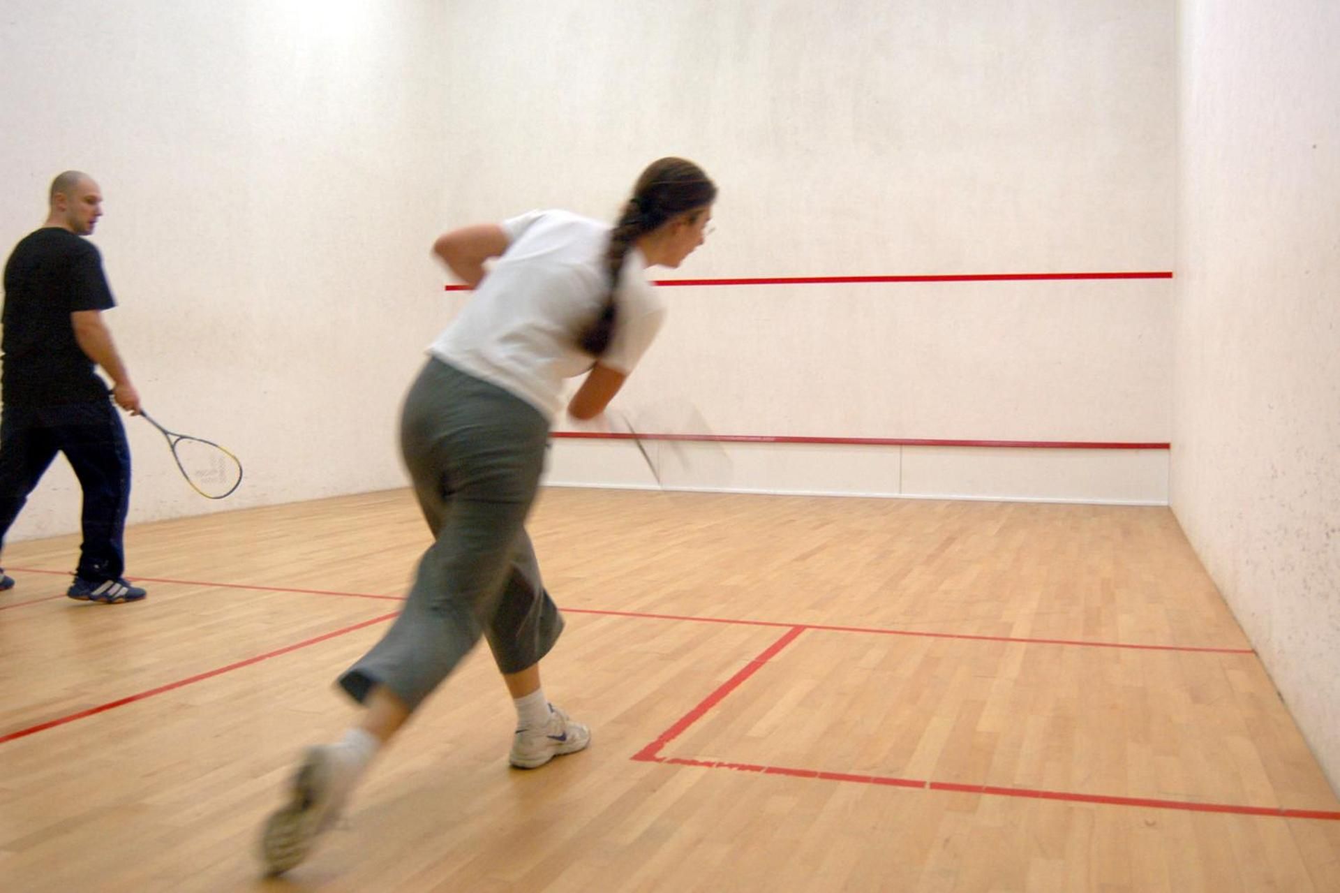 Una palestra per squash con pavimento in legno e linee di delimitazione rosse.