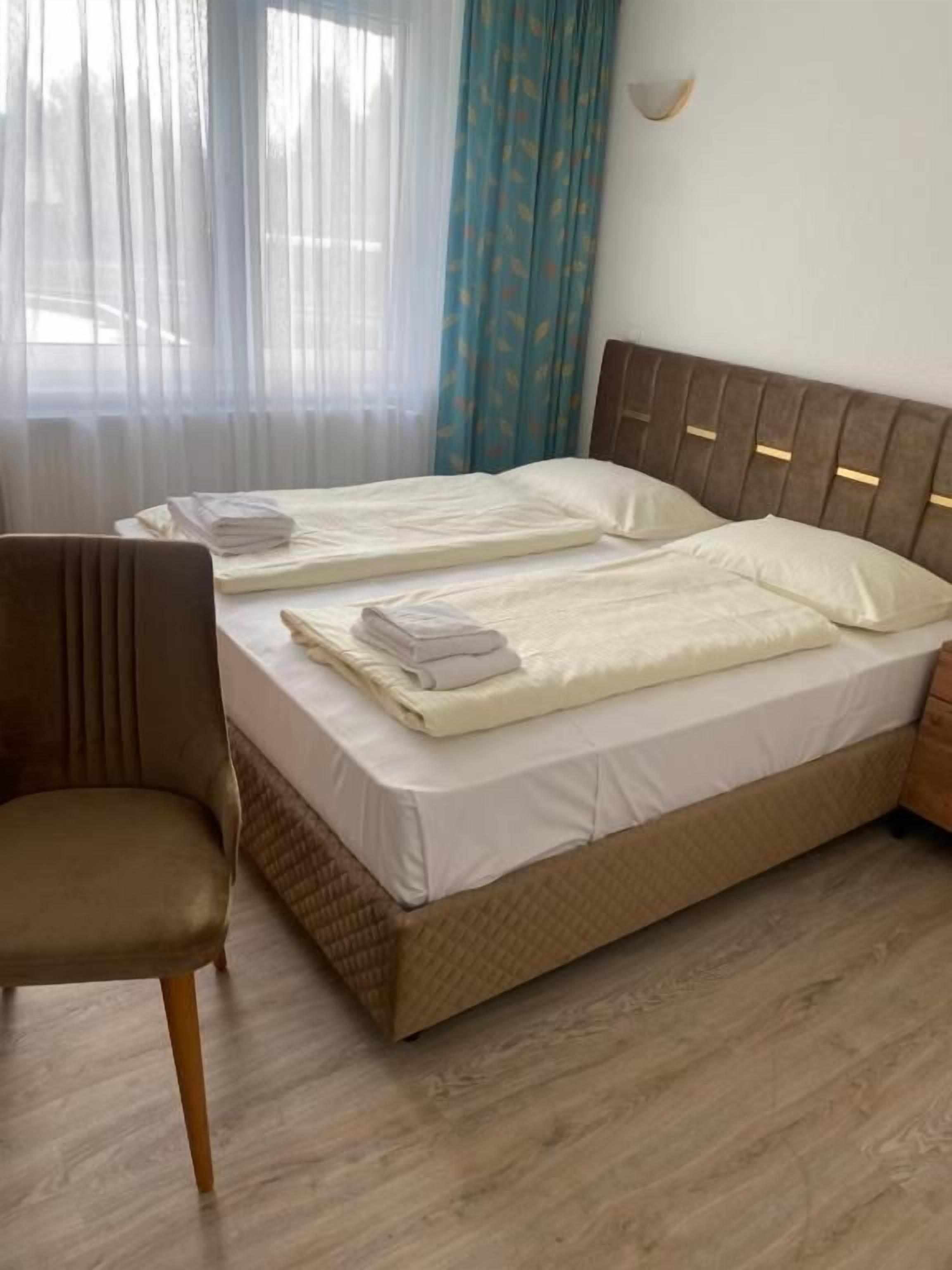 A double bed with a headboard, a chair, and a window with sheer curtains.