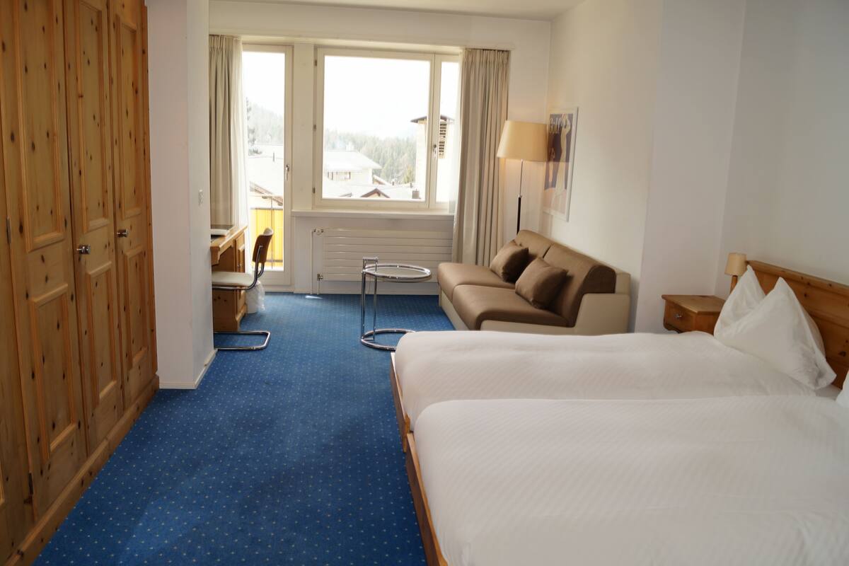 Une chambre d’hôtel avec un grand lit, un canapé, une petite table et une vue sur une montagne par la fenêtre.