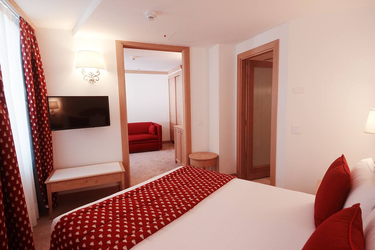 Une chambre d’hôtel avec un lit, une télévision, un bureau, une chaise, une couvre-lit à motifs rouges et un canapé rouge en arrière-plan.