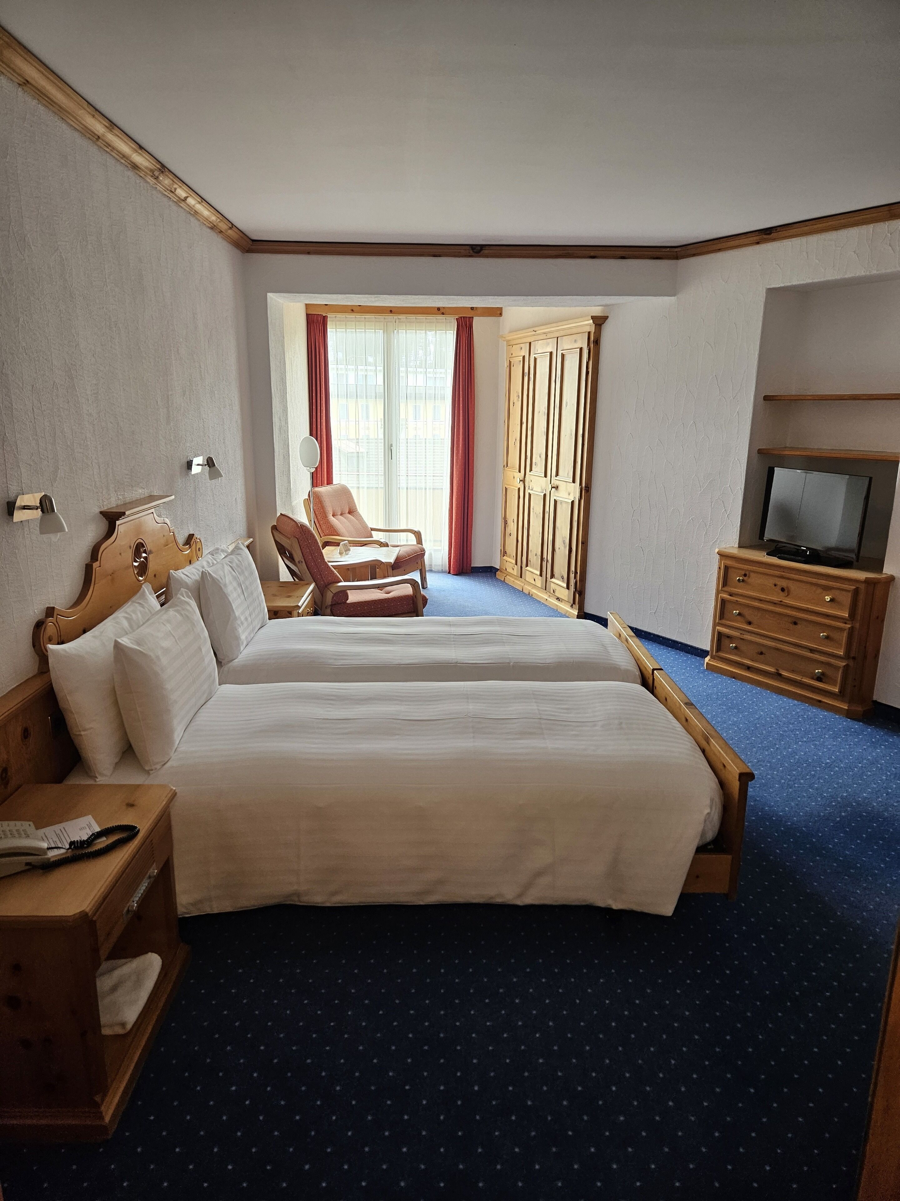 A hotel room with a large bed, a chair, a TV, and a wardrobe.