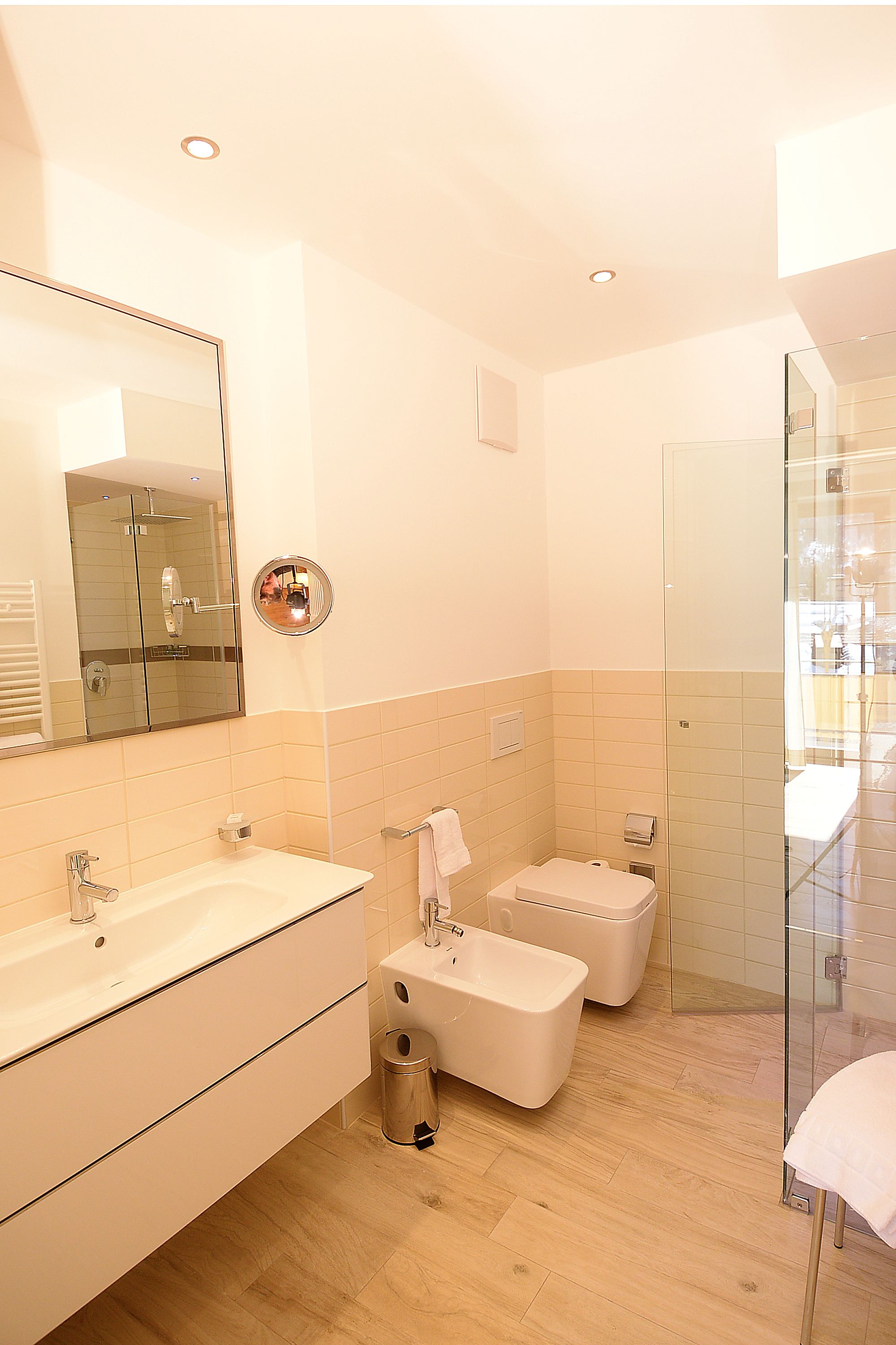 Een moderne badkamer met een grote spiegel, twee wastafels, een douche en een douchecel met glazen wanden.