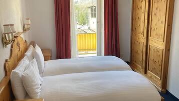 Ein Doppelbett mit weißer Bettwäsche, ein hölzernes Kopfteil, ein Nachttisch mit Telefon und ein Fenster mit roten Vorhängen.