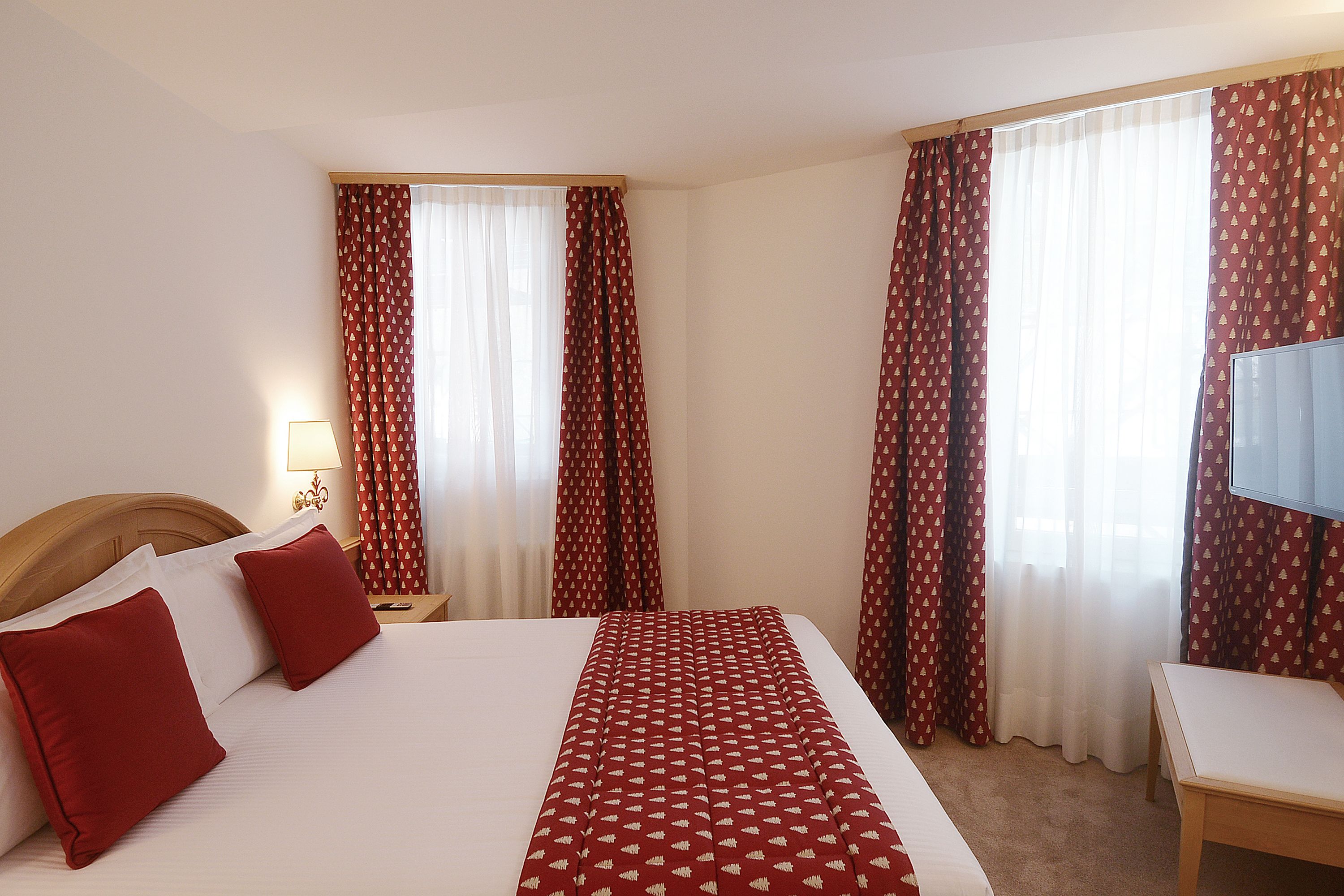 A hotel room with a bed, a bedside table with a lamp, a TV, and curtains.